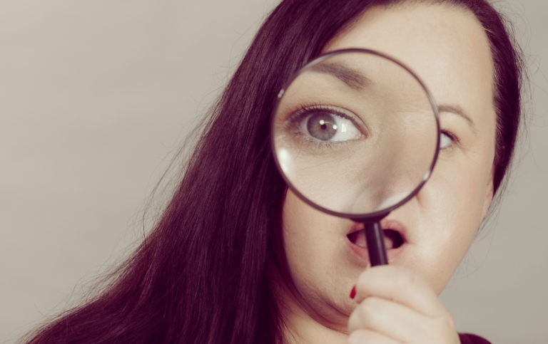 Kvinna som håller ett förstoringsglas framför ena ögat